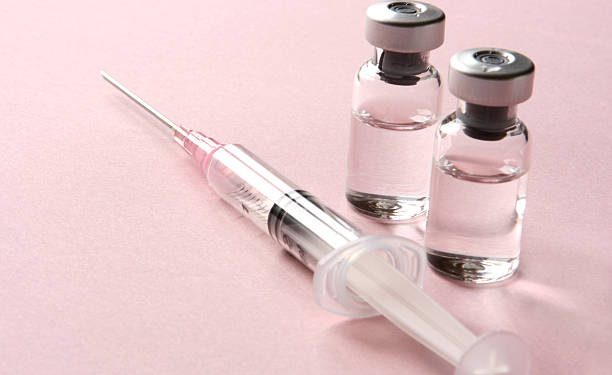 This is a studio shot of two glass vials with medicine and a single syringe ready for an injection or vaccination on a light pink background with copy space. The vials and syringe could represent various healthcare and medicine concepts.